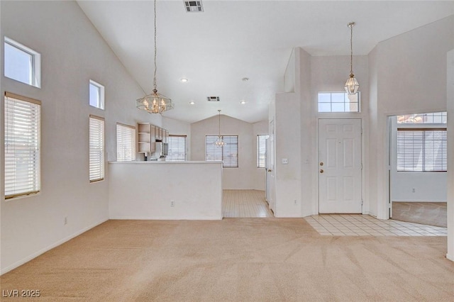 entrance foyer featuring an inviting chandelier, light colored carpet, high vaulted ceiling, and visible vents