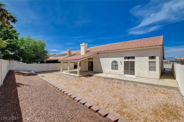 rear view of house featuring a tile roof, a patio, stucco siding, a fenced backyard, and a chimney