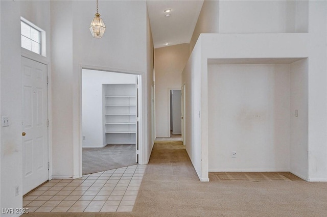 foyer featuring light carpet, a high ceiling, baseboards, and light tile patterned floors