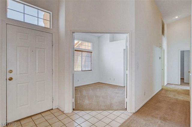 entryway featuring light tile patterned floors, baseboards, light colored carpet, and a towering ceiling