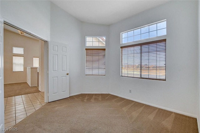 tiled spare room featuring carpet flooring, baseboards, and a towering ceiling