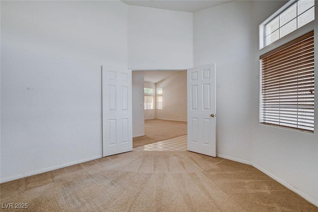carpeted spare room featuring baseboards and a towering ceiling