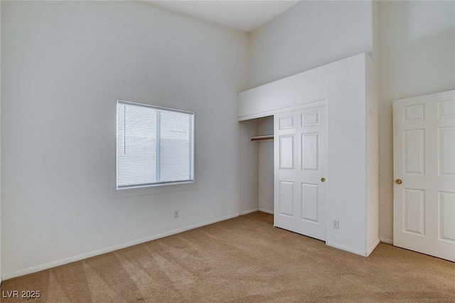 unfurnished bedroom with baseboards, a closet, carpet floors, and a towering ceiling
