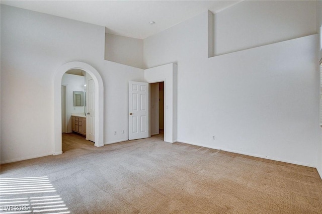unfurnished bedroom featuring light carpet, baseboards, and arched walkways
