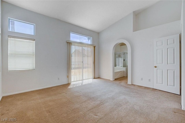 empty room featuring arched walkways, baseboards, high vaulted ceiling, and light colored carpet