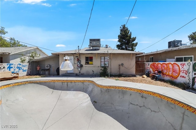 view of front of house with cooling unit, an empty pool, and fence