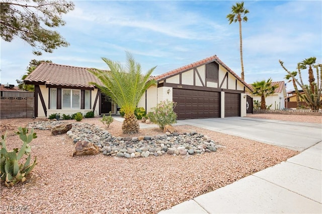 view of front of house featuring an attached garage, a tiled roof, stucco siding, fence, and driveway