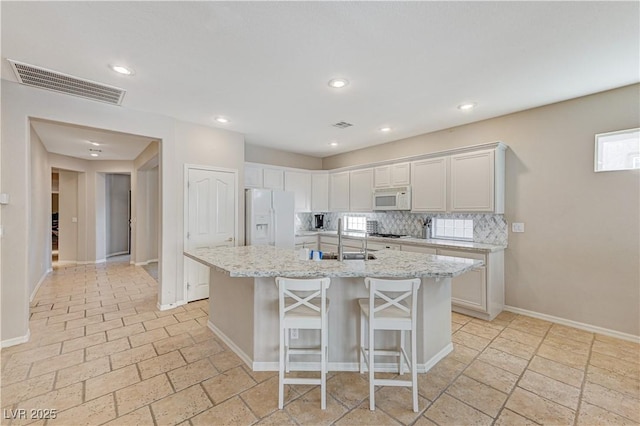 kitchen featuring white appliances, a sink, a center island with sink, a kitchen bar, and baseboards