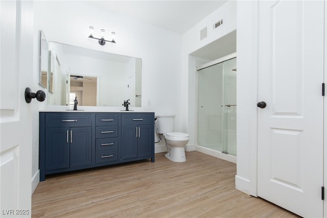 bathroom featuring toilet, wood finished floors, a stall shower, and double vanity