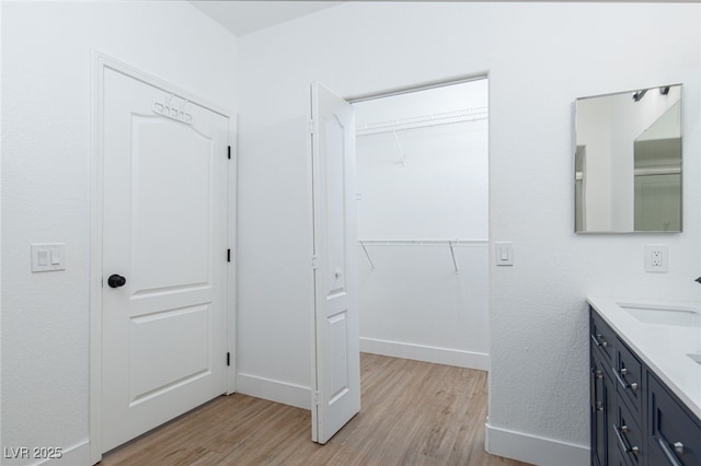 bathroom featuring wood finished floors, double vanity, baseboards, and a spacious closet
