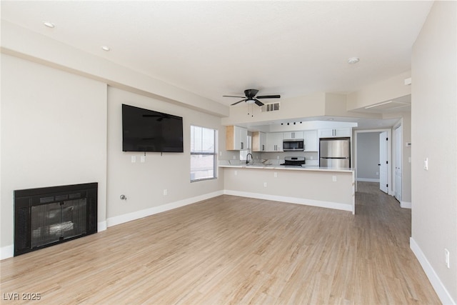 unfurnished living room featuring ceiling fan, light wood-type flooring, a glass covered fireplace, baseboards, and a sink