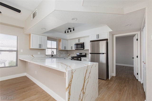 kitchen with stainless steel appliances, a sink, a peninsula, baseboards, and light wood-type flooring
