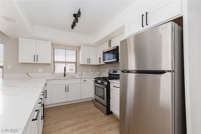 kitchen with appliances with stainless steel finishes, a sink, white cabinetry, and light stone counters
