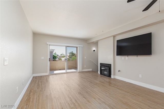 unfurnished living room featuring a ceiling fan, light wood finished floors, a glass covered fireplace, and baseboards