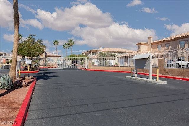view of asphalt road featuring curbs, a gate, a residential view, and a gated entry