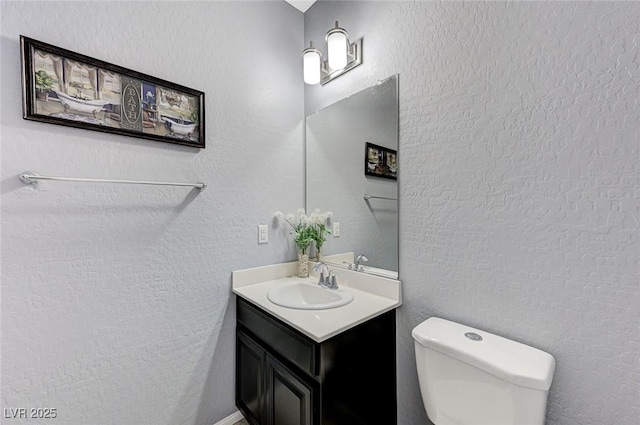 bathroom featuring vanity, toilet, and a textured wall