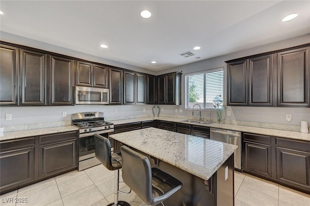 kitchen with a sink, a kitchen breakfast bar, light stone counters, light tile patterned floors, and appliances with stainless steel finishes