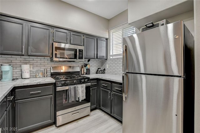 kitchen featuring light wood-type flooring, stainless steel appliances, backsplash, and light stone counters
