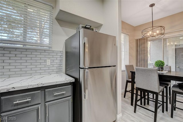 kitchen featuring freestanding refrigerator, a wealth of natural light, light stone countertops, a chandelier, and tasteful backsplash