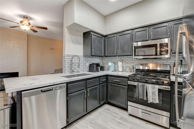 kitchen featuring a sink, a peninsula, stainless steel appliances, light stone counters, and a ceiling fan