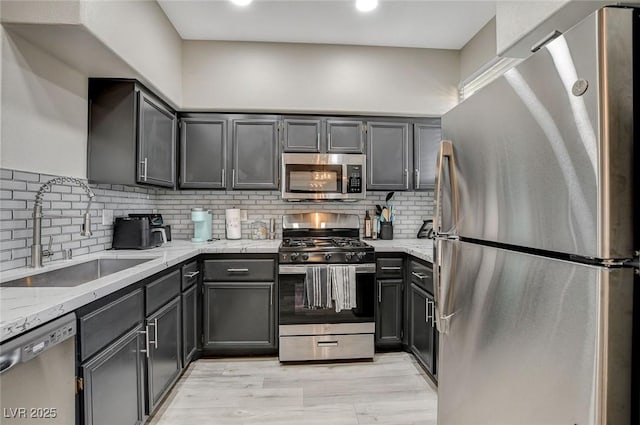 kitchen with light stone countertops, light wood-style flooring, a sink, decorative backsplash, and appliances with stainless steel finishes