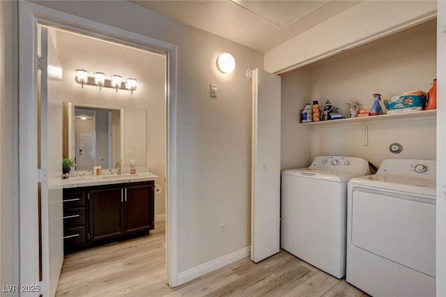 clothes washing area with a sink, laundry area, washing machine and clothes dryer, light wood-type flooring, and baseboards
