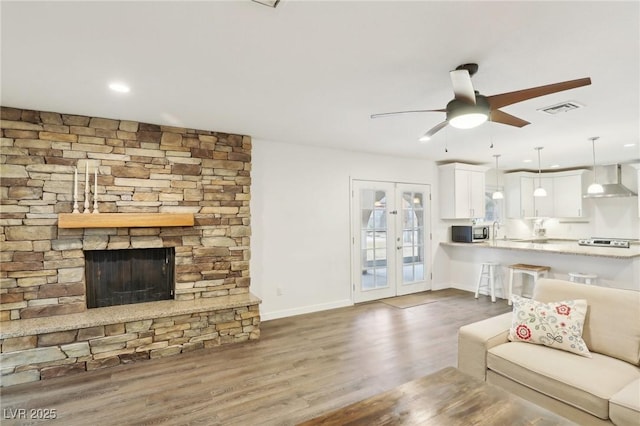 3155 Duneville St, Las Vegas, NV 89146 - living room with wood finished floors, visible vents, a ceiling fan, baseboards, and a stone fireplace