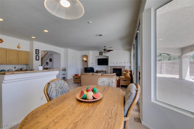 dining space with ceiling fan, arched walkways, a tiled fireplace, light tile patterned floors, and recessed lighting