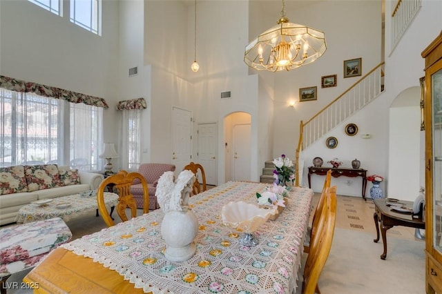 dining room with arched walkways, a high ceiling, a chandelier, stairs, and light colored carpet