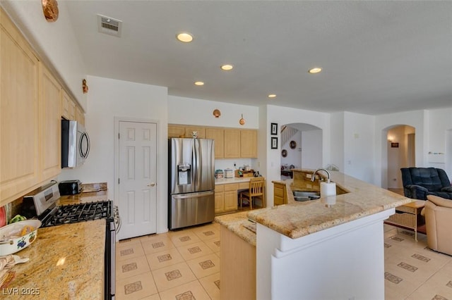 kitchen with stainless steel appliances, a sink, arched walkways, light brown cabinetry, and open floor plan