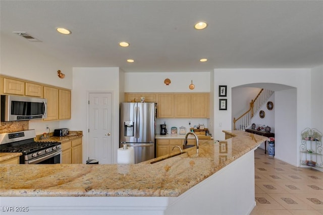 kitchen featuring appliances with stainless steel finishes, a sink, light brown cabinetry, light stone countertops, and recessed lighting
