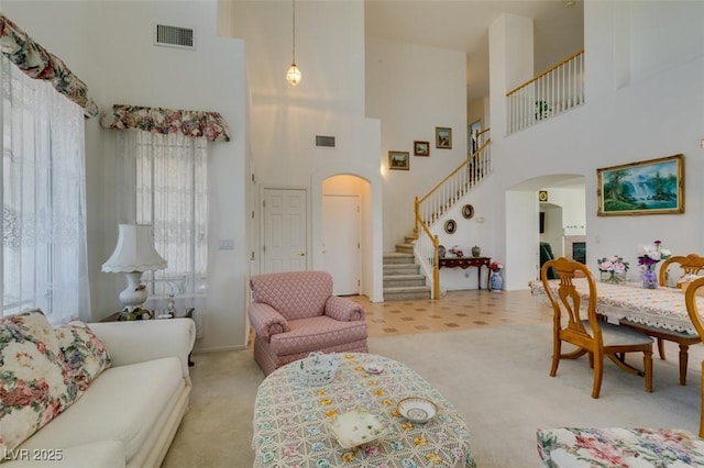 carpeted living room featuring arched walkways, stairs, and a towering ceiling