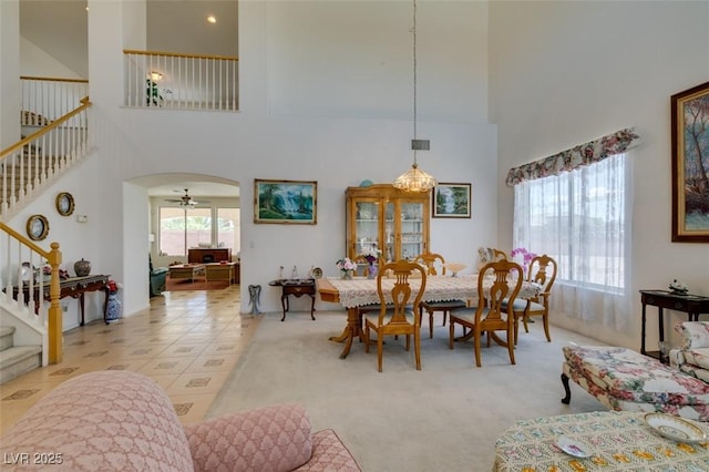 dining space featuring a towering ceiling, stairway, and arched walkways
