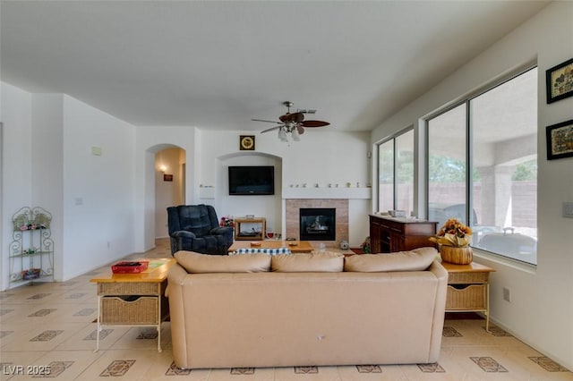 living area with arched walkways, ceiling fan, a fireplace, and light tile patterned flooring