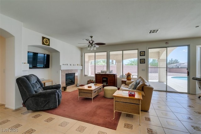 living area featuring ceiling fan, a tiled fireplace, light tile patterned floors, and arched walkways