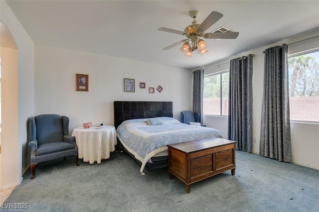 bedroom featuring arched walkways, multiple windows, light carpet, and ceiling fan