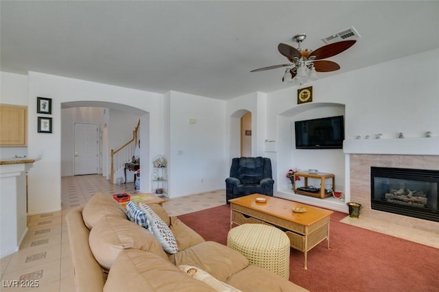 living room with arched walkways, a ceiling fan, a high end fireplace, and stairs