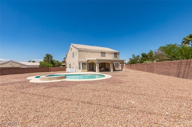 back of house with stucco siding, a tile roof, a pool with connected hot tub, and a fenced backyard