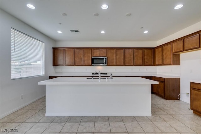 528 Sunny Pointe St, Henderson, NV 89011 - kitchen with stainless steel microwave, a center island with sink, a sink, light countertops, and brown cabinets