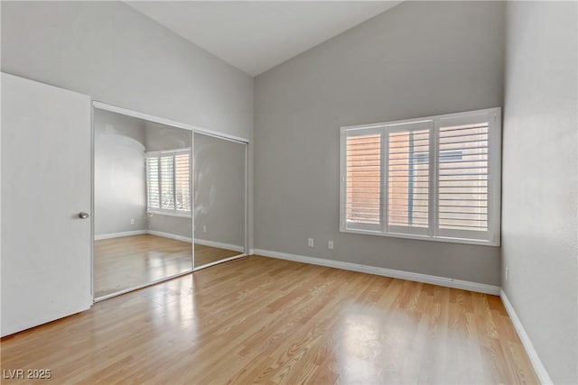 unfurnished bedroom with baseboards, a closet, high vaulted ceiling, and wood finished floors