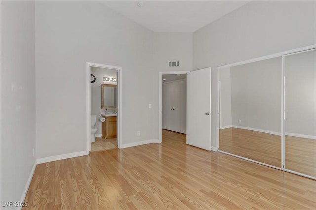 unfurnished bedroom featuring a closet, baseboards, visible vents, a towering ceiling, and light wood-style floors