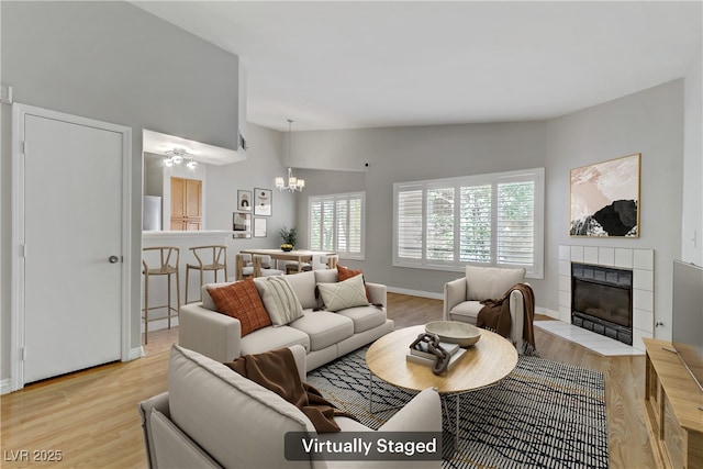 living area featuring light wood finished floors, baseboards, a tile fireplace, and a notable chandelier