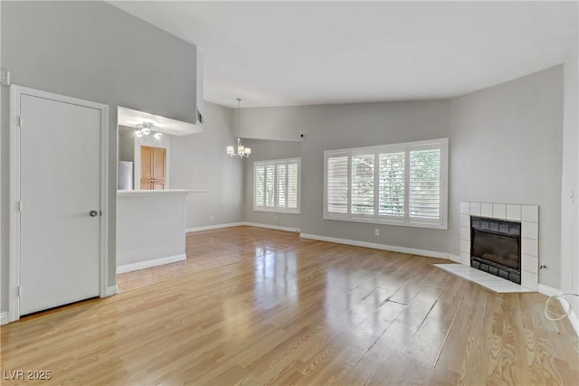 unfurnished living room featuring a fireplace, a notable chandelier, baseboards, and wood finished floors