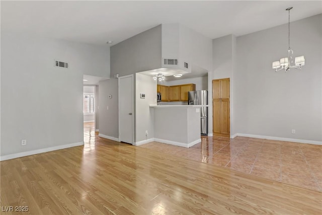 unfurnished living room featuring a notable chandelier, visible vents, baseboards, and high vaulted ceiling