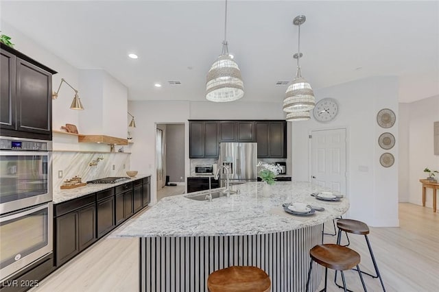 kitchen featuring backsplash, appliances with stainless steel finishes, light wood-style flooring, and a sink