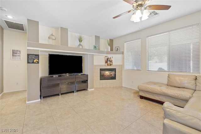 living area with a ceiling fan, baseboards, a tile fireplace, and visible vents