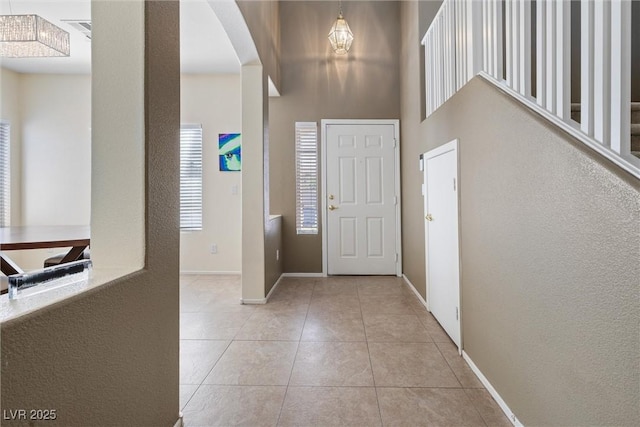 entryway featuring light tile patterned flooring, arched walkways, baseboards, and a towering ceiling
