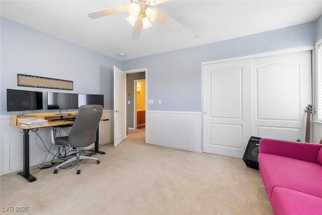 carpeted office space featuring a wainscoted wall and a ceiling fan