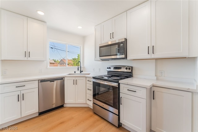 kitchen featuring a sink, white cabinets, light wood-type flooring, appliances with stainless steel finishes, and recessed lighting