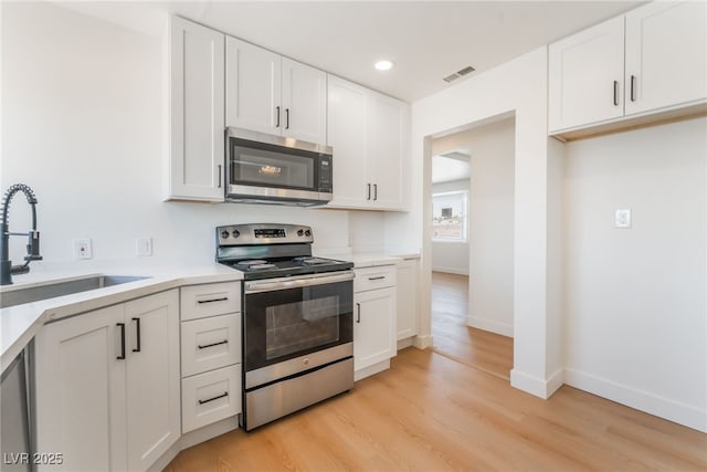 kitchen featuring stainless steel appliances, visible vents, a sink, light countertops, and white cabinets